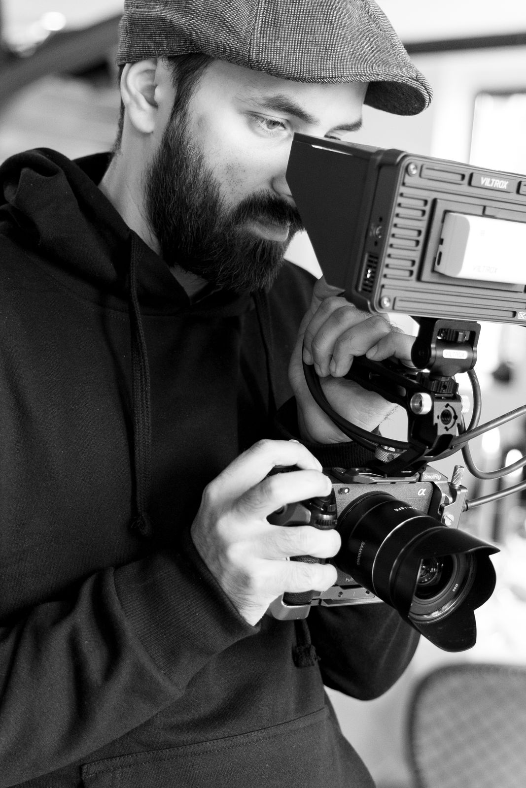 Ein Mann mit Bart und Schiebermütze filmt mit einer Kamera mit externem Monitor.