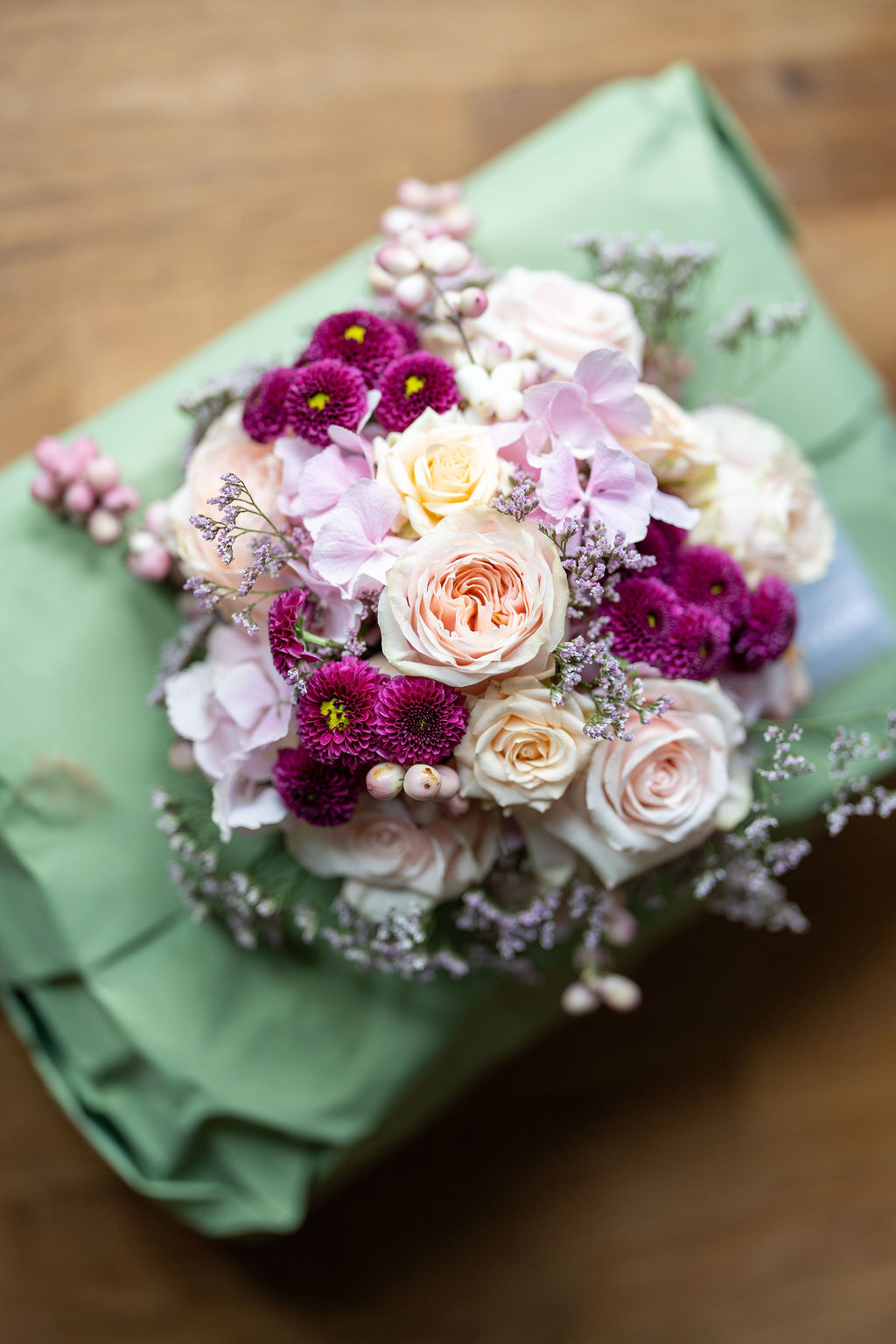 Nahaufnahme eines Hochzeitsstraußes aus Rosen, Chrysanthemen und Schleierkraut in Rosa und Lila auf grünem Papier.