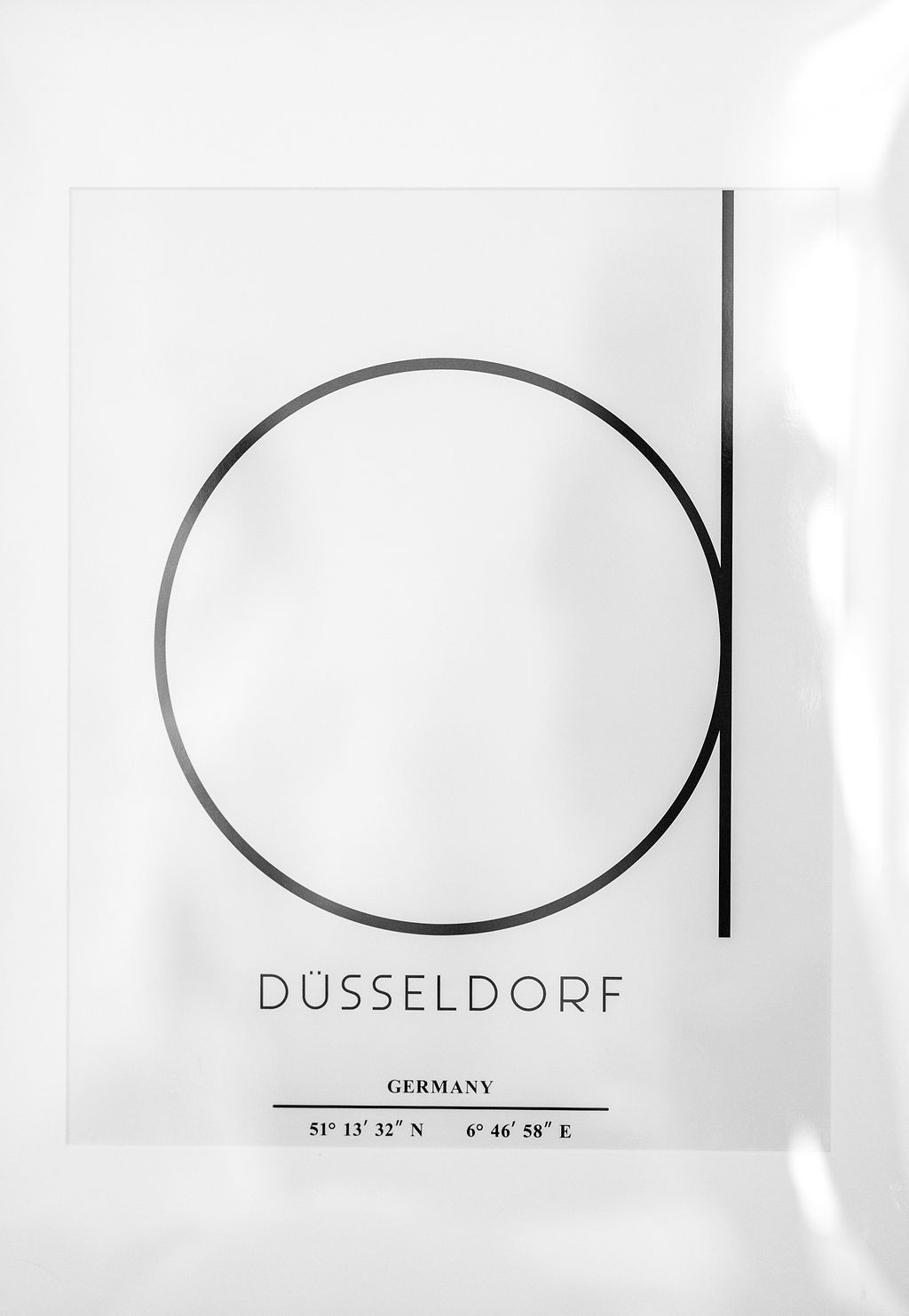 Ein weißes Poster mit schwarzem Kreis und Schriftzug "DÜSSELDORF" und Koordinaten.