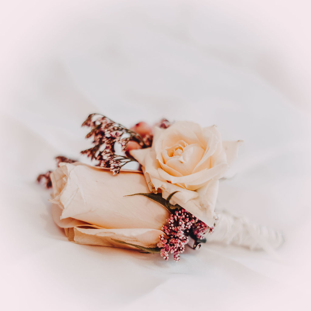 Ansteckblume mit zwei cremefarbenen Rosen und kleineren, rötlichen Blüten auf weißem Stoff.