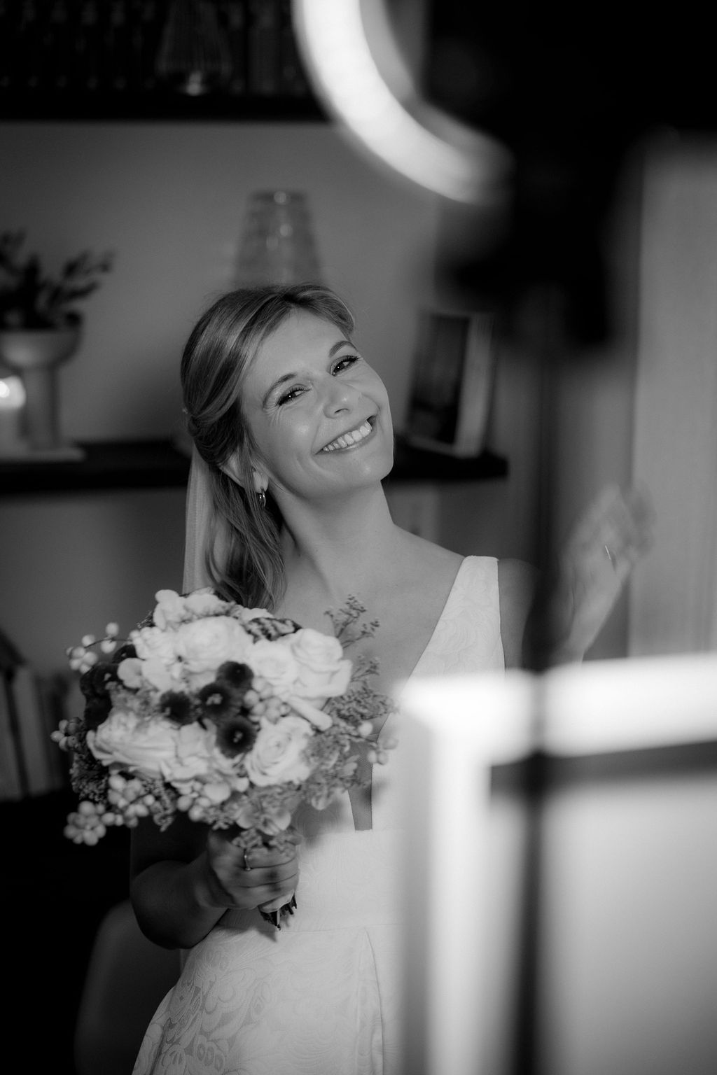 Eine lächelnde Frau in einem Hochzeitskleid hält einen Blumenstrauß. Das Foto ist in Schwarz-Weiß.
