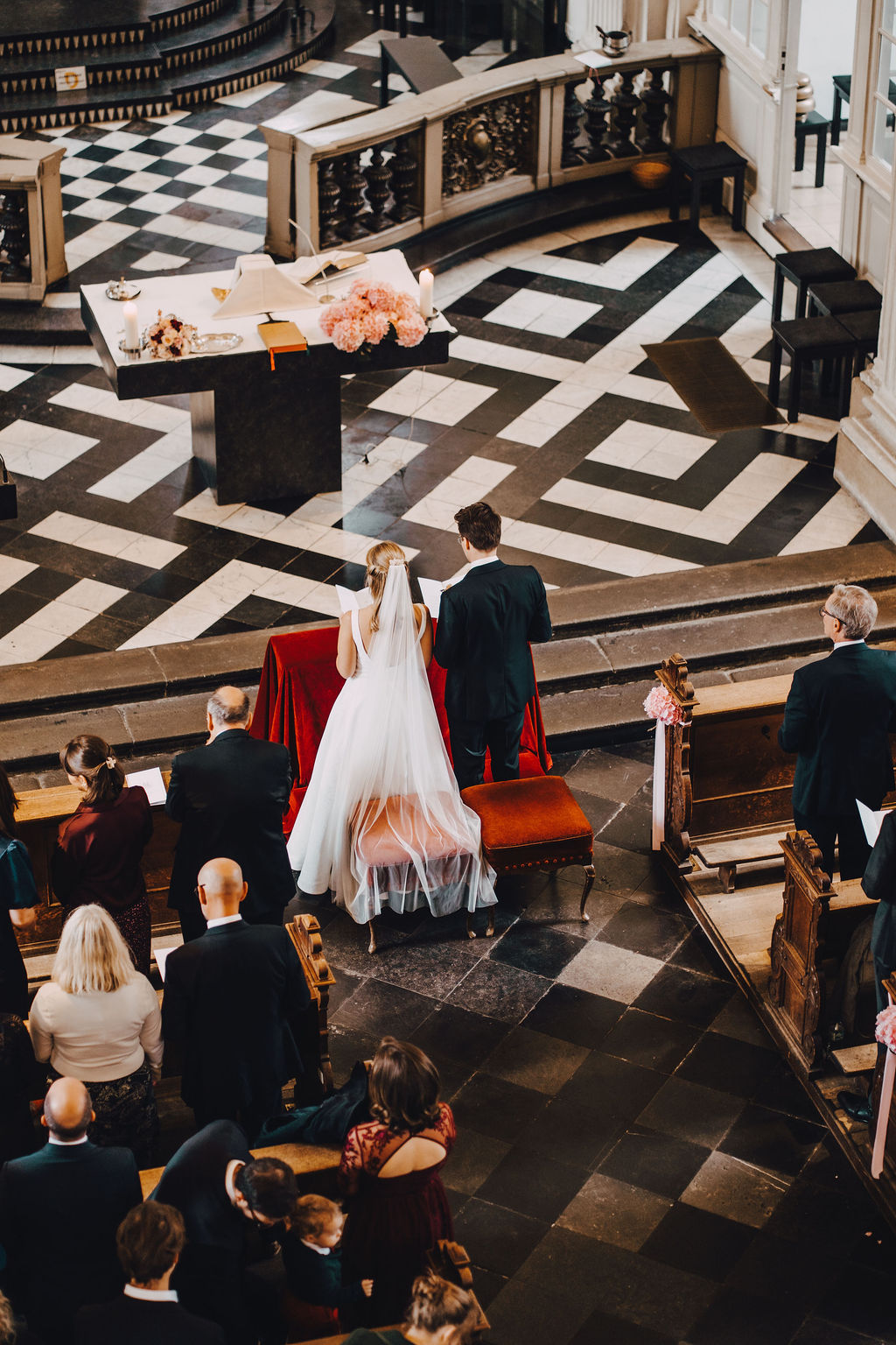 Brautpaar und Hochzeitsgäste in einer Kirche während der Zeremonie, von oben fotografiert.