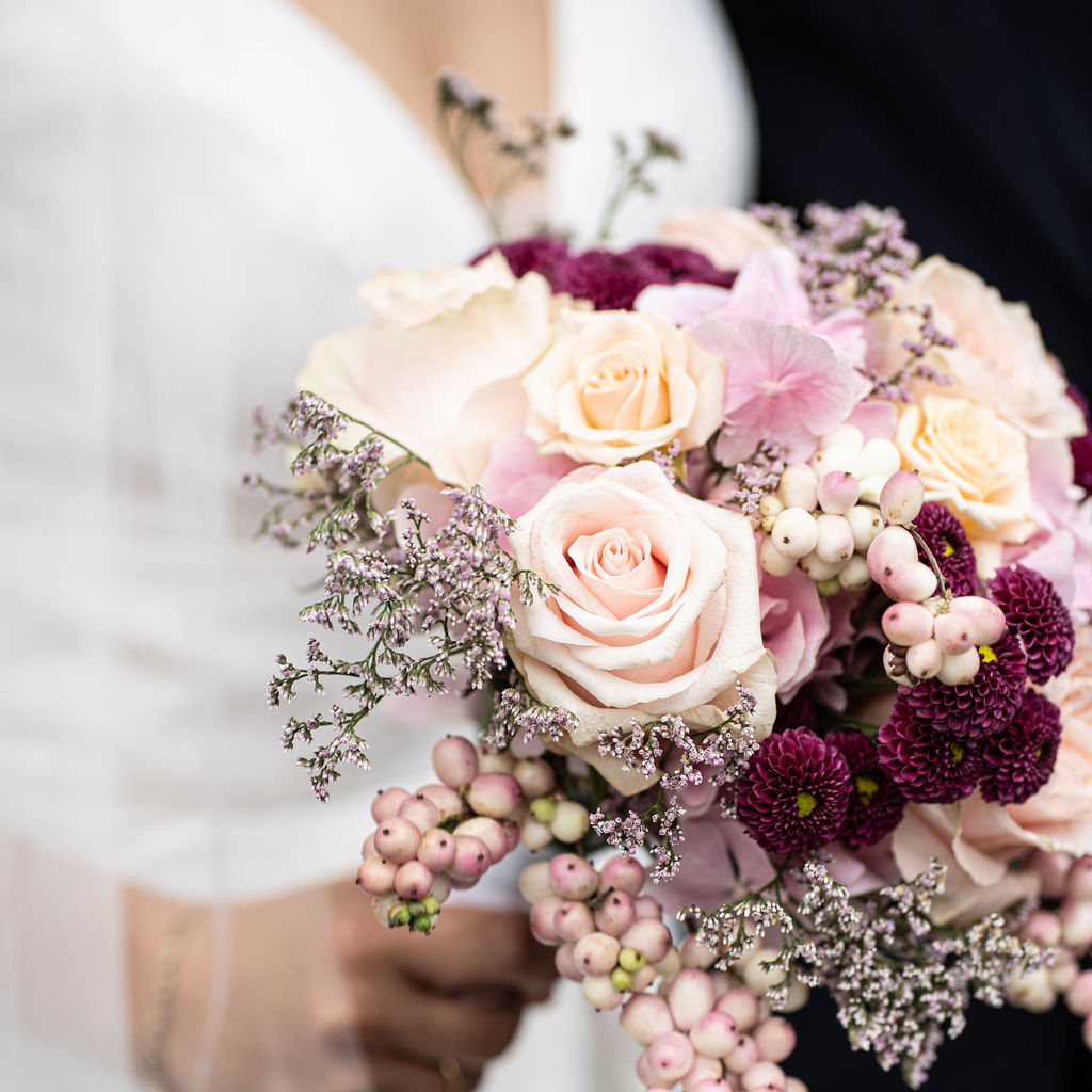 Nahaufnahme eines Hochzeitsstraußes mit rosa Rosen, roten Dahlien und rosa Beeren.