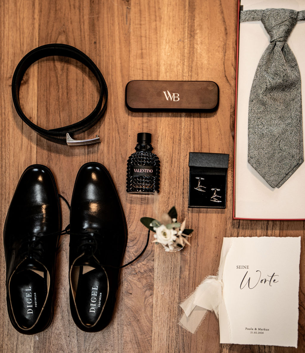 Hochzeitsaccessoires für den Bräutigam auf Holzboden, inklusive Schuhe, Gürtel, Krawatte, Manschettenknöpfe und Anstecker.