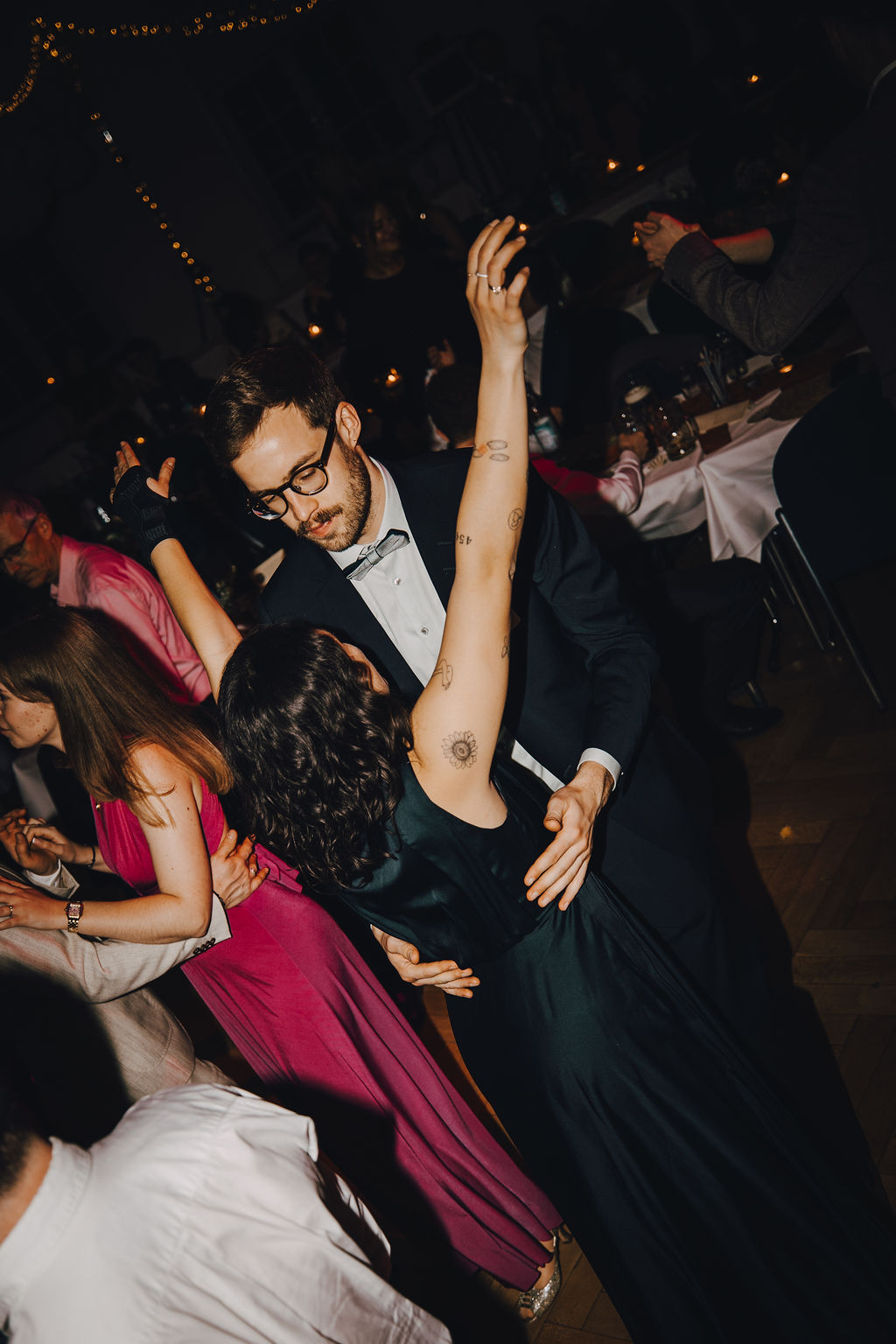 Ein Mann im Anzug tanzt mit einer Frau im dunklen Kleid. Ihre Arme sind erhoben, seine Hände an ihrer Taille.