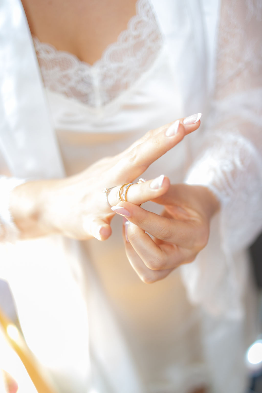 Eine Frau schiebt sich einen goldenen Ring auf den Finger. Sie trägt einen weißen Morgenmantel mit Spitze.