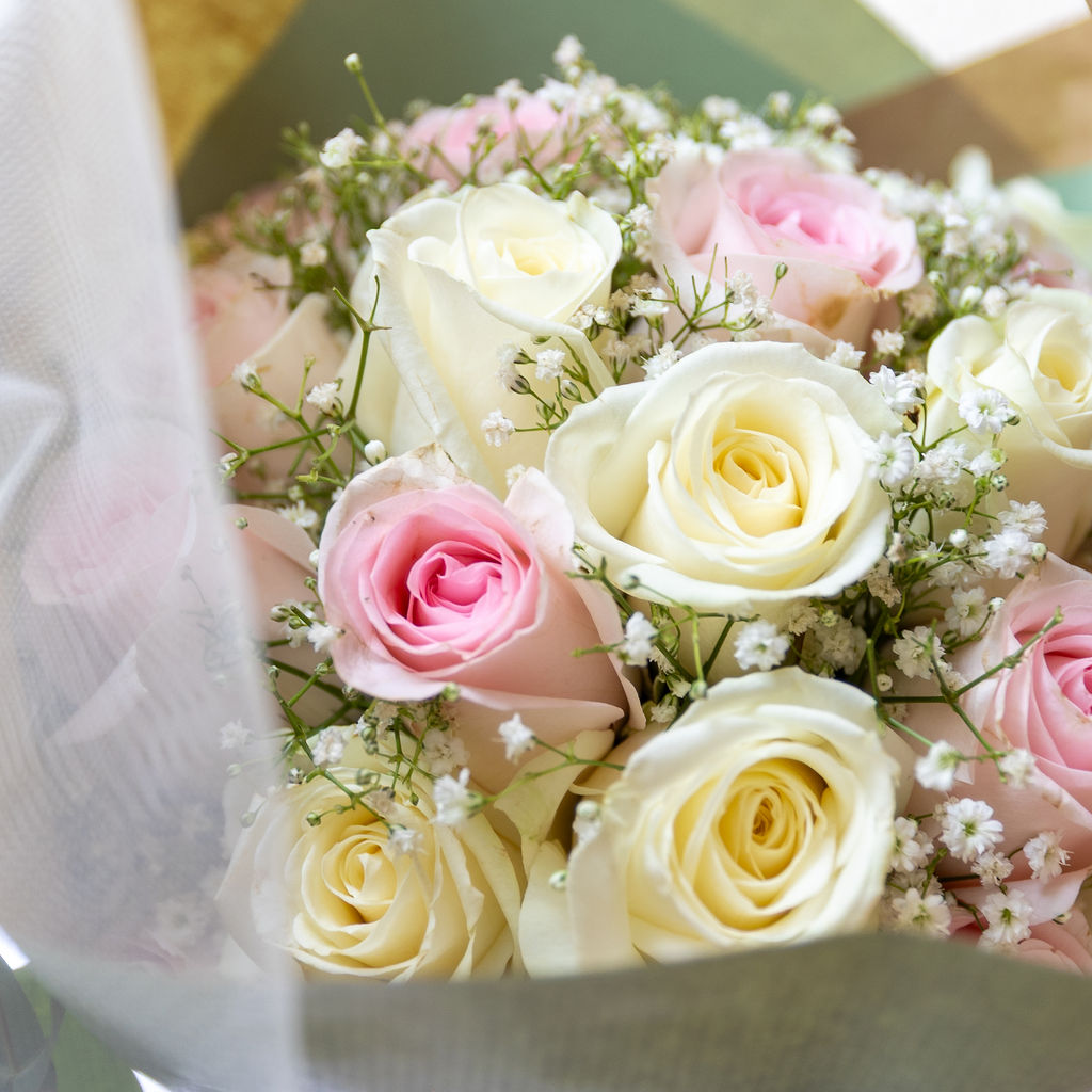 Nahaufnahme eines Brautstraußes mit weißen und rosa Rosen und Schleierkraut, umwickelt mit weißem Stoff.