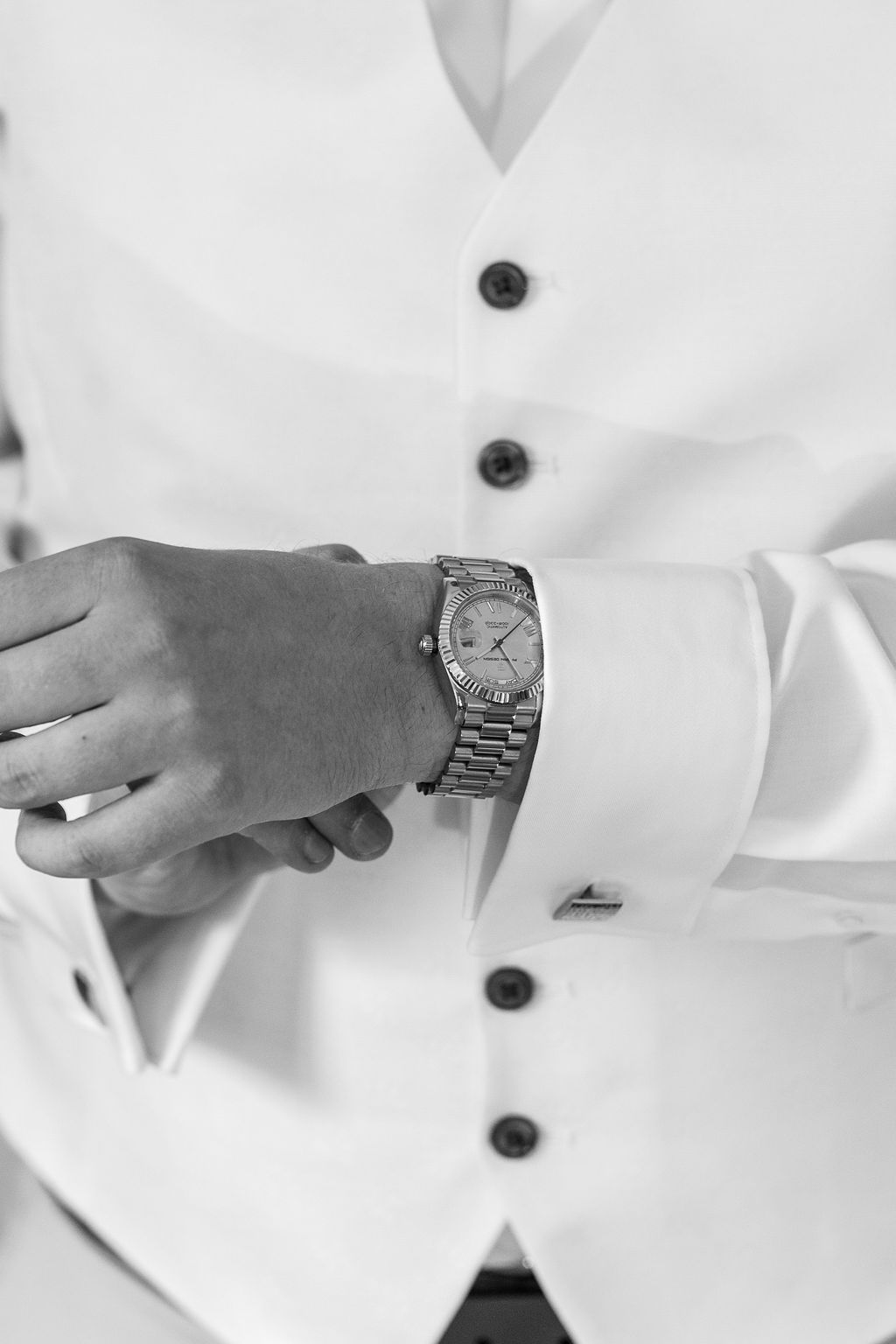Eine silberne Armbanduhr an einem Handgelenk mit Manschettenhemd und Weste.