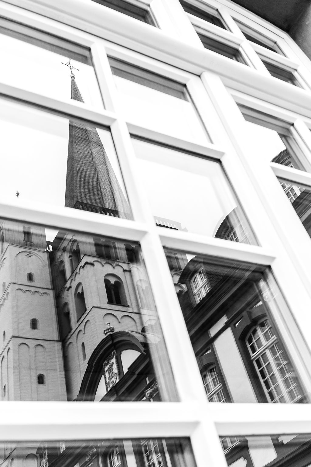 Reflexion eines Kirchturms mit Kreuz und eines historischen Gebäudes in einem Fensterrahmen.