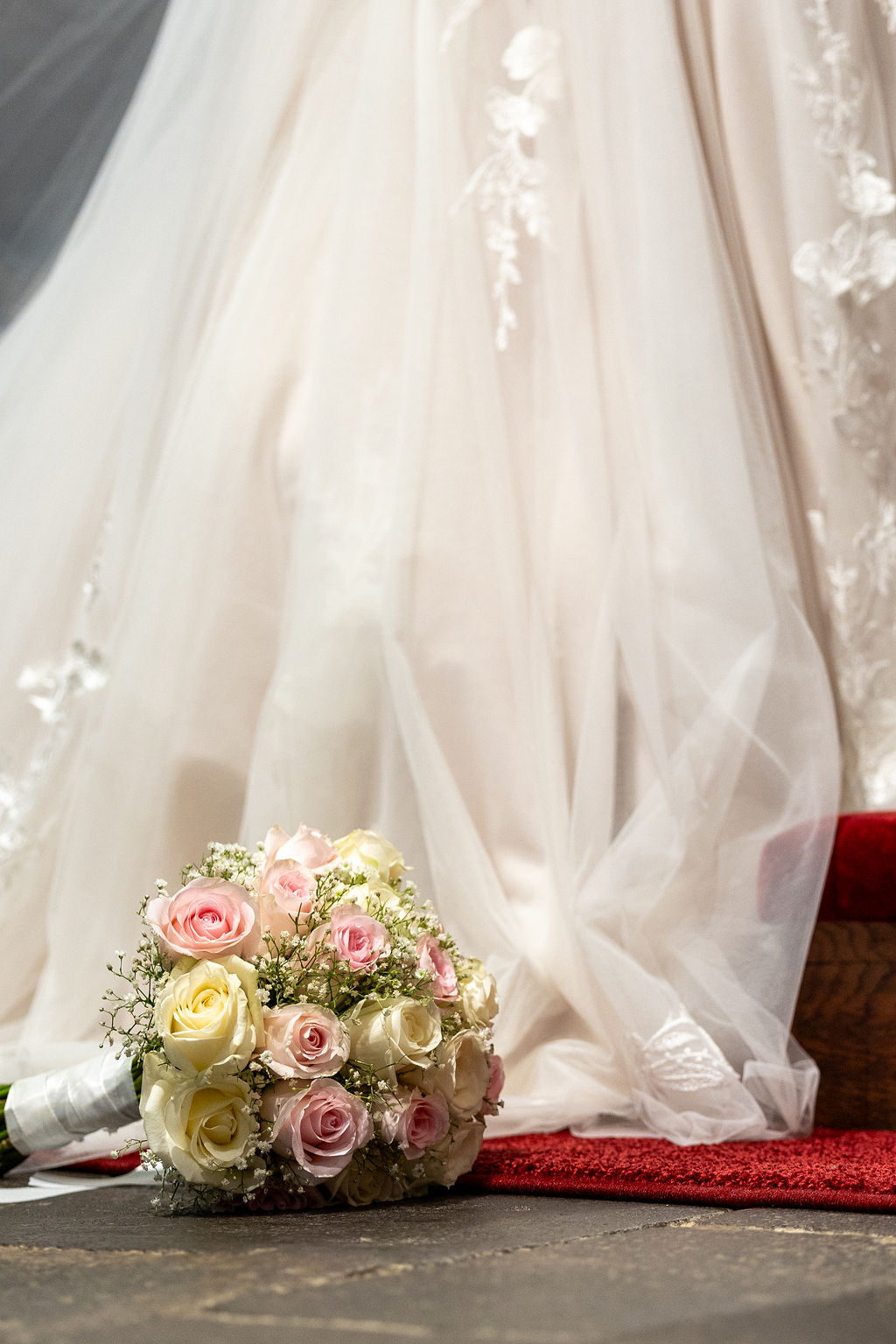 Brautstrauß mit hellrosafarbenen und cremefarbenen Rosen und Schleierkraut liegt vor weißem Brautkleid auf dem Boden.