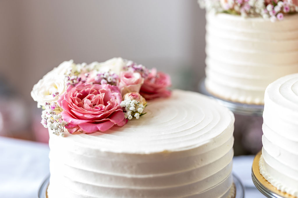 Eine gestufte Hochzeitstorte mit weißen und rosafarbenen Blumen, umgeben von zwei weiteren weißen Torten.