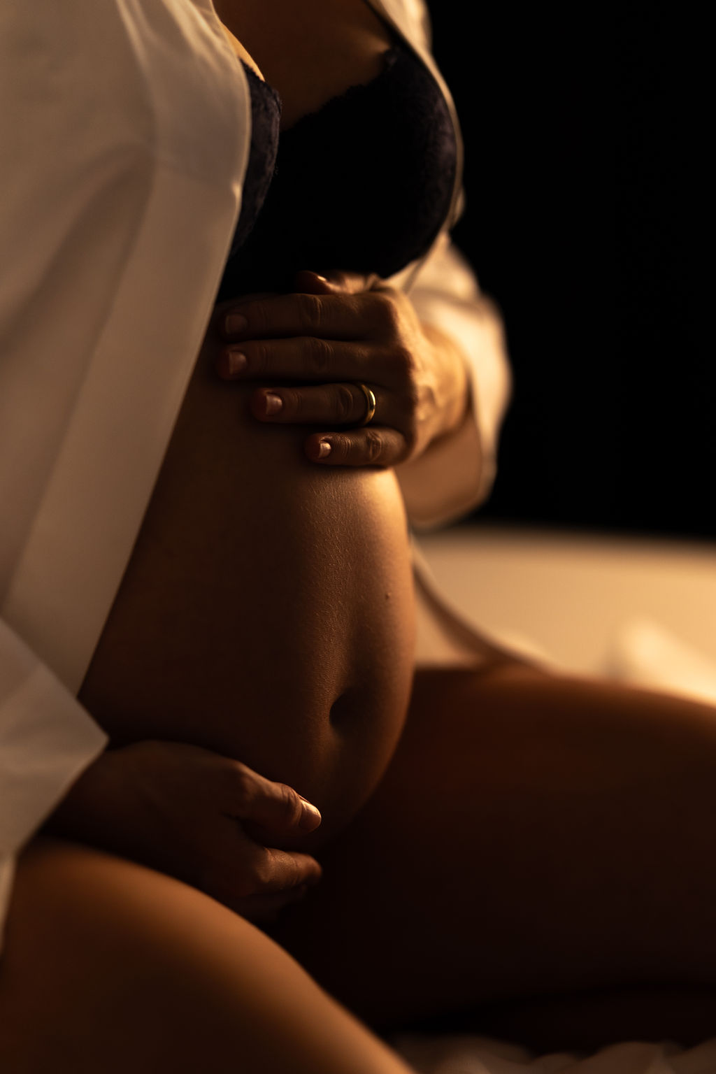 Eine schwangere Person hält ihren Bauch, auf dem Finger ein Ring, dunkler Hintergrund.