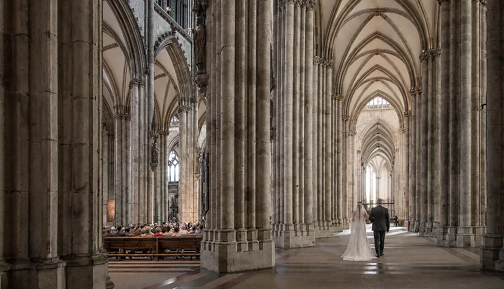 Ein Brautpaar geht durch das Kirchenschiff einer Kathedrale mit hohen Säulen und Gewölbedecken.