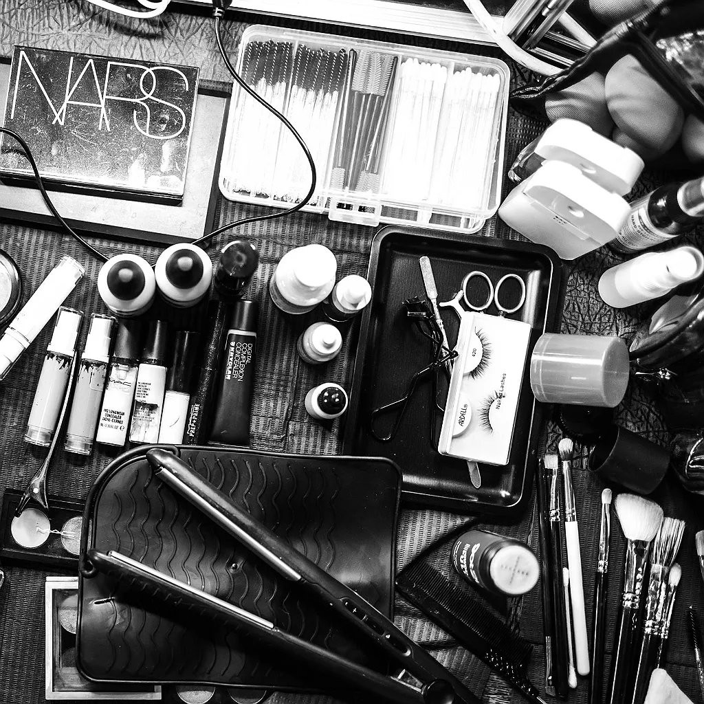 Verschiedene Make-up-Produkte, Pinsel, Wimpern, ein Glätteisen und Zubehör liegen auf einem dunklen Untergrund.