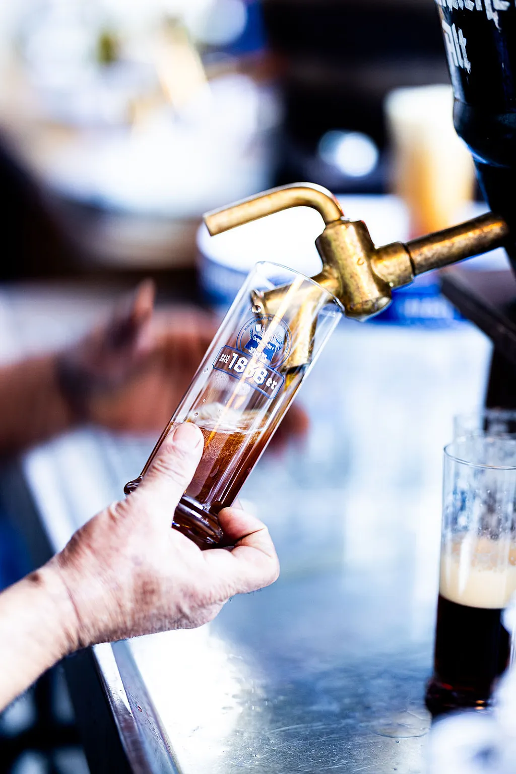 Eine Hand füllt ein Bierglas mit dunklem Bier aus einem Zapfhahn an einem Tresen.