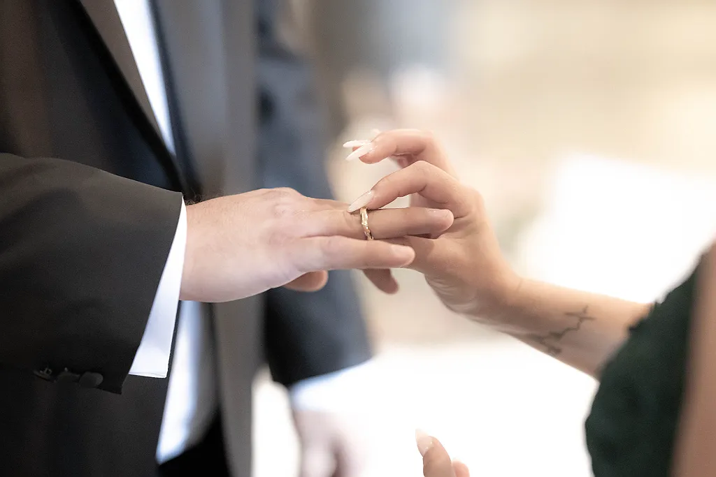 Eine Person schiebt einer anderen Person einen goldenen Ehering auf den Finger.