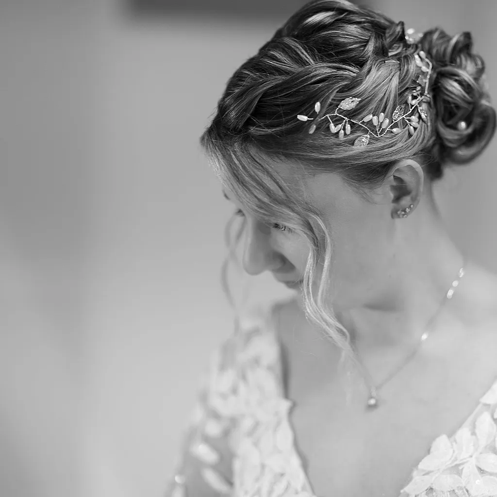 Seitenansicht einer Braut mit Hochsteckfrisur, Haarschmuck, Ohrring und einer Halskette im Vordergrund.