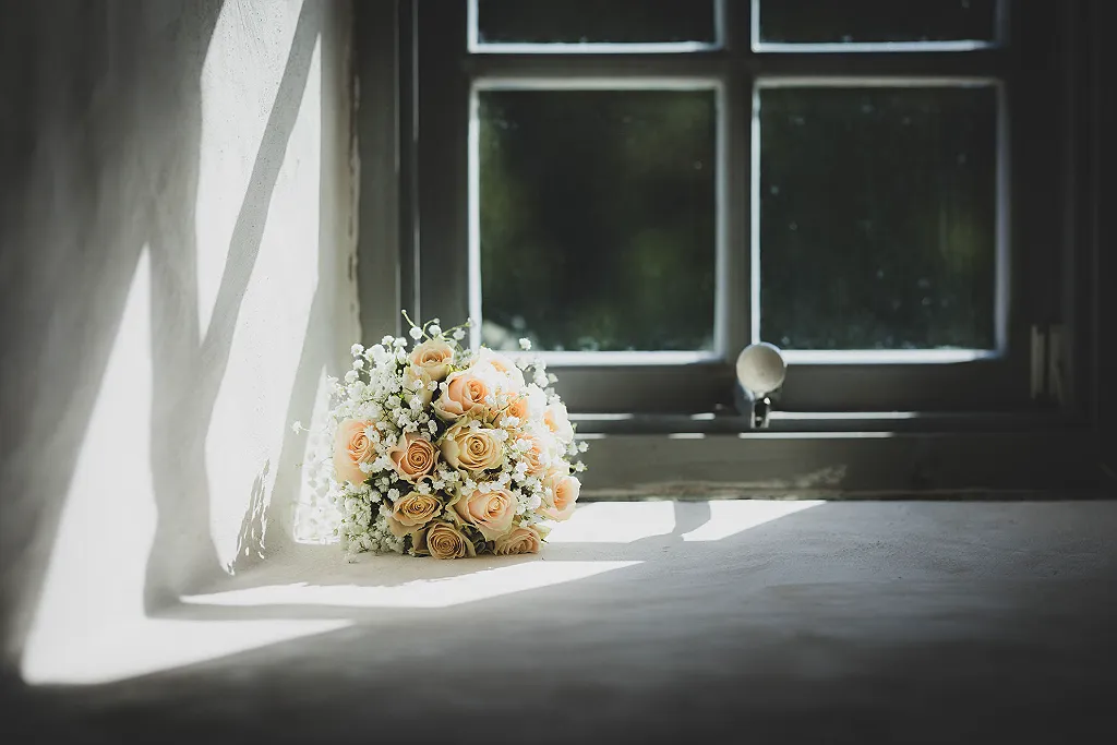 Hochzeitsstrauß mit pfirsichfarbenen Rosen und Schleierkraut auf einer Fensterbank, im Schatten und Sonnenlicht.