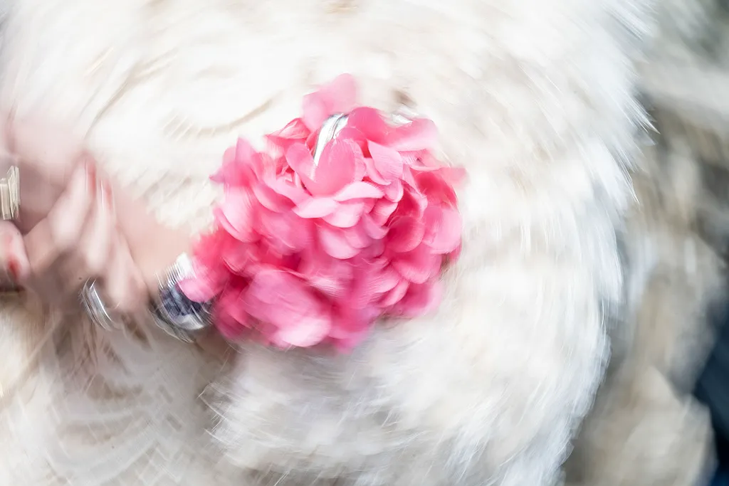 Ein verschwommenes Bild der Hände einer Person, die einen rosa Blumenstrauß auf einem fellartigen Hintergrund halten.