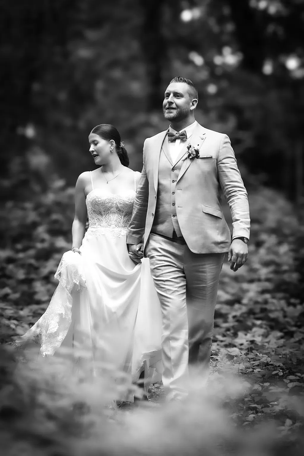 Brautpaar in Hochzeitskleidung geht Hand in Hand auf einem von Blättern bedeckten Weg.