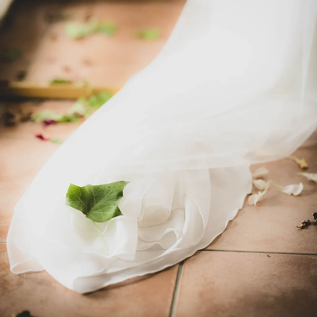 Ein grünes Blatt liegt auf dem weißen Stoff eines Hochzeitskleides, das auf einem braunen Fliesenboden liegt.
