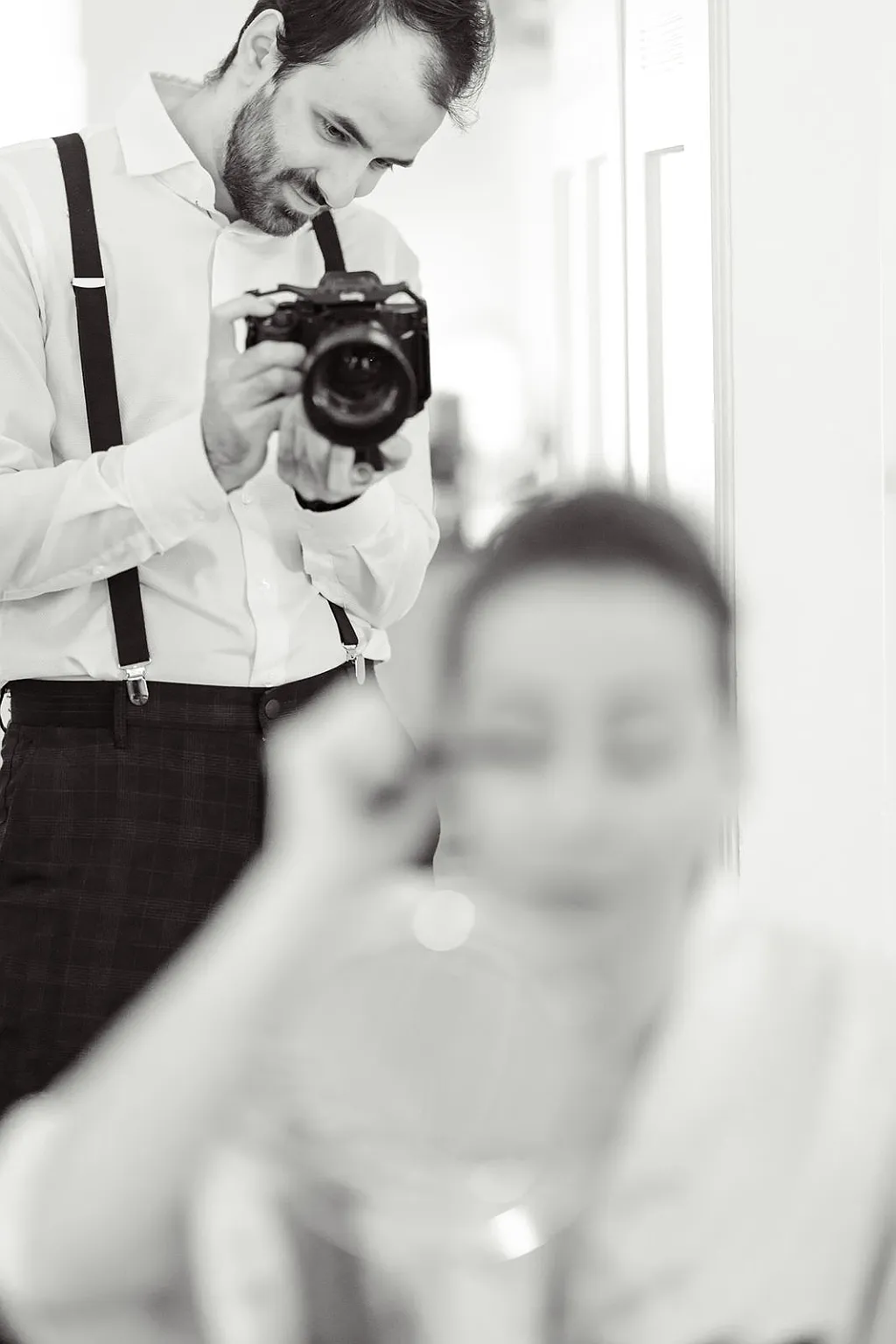 Ein Mann mit Hosenträgern fotografiert eine unscharfe Person, die sich schminkt.