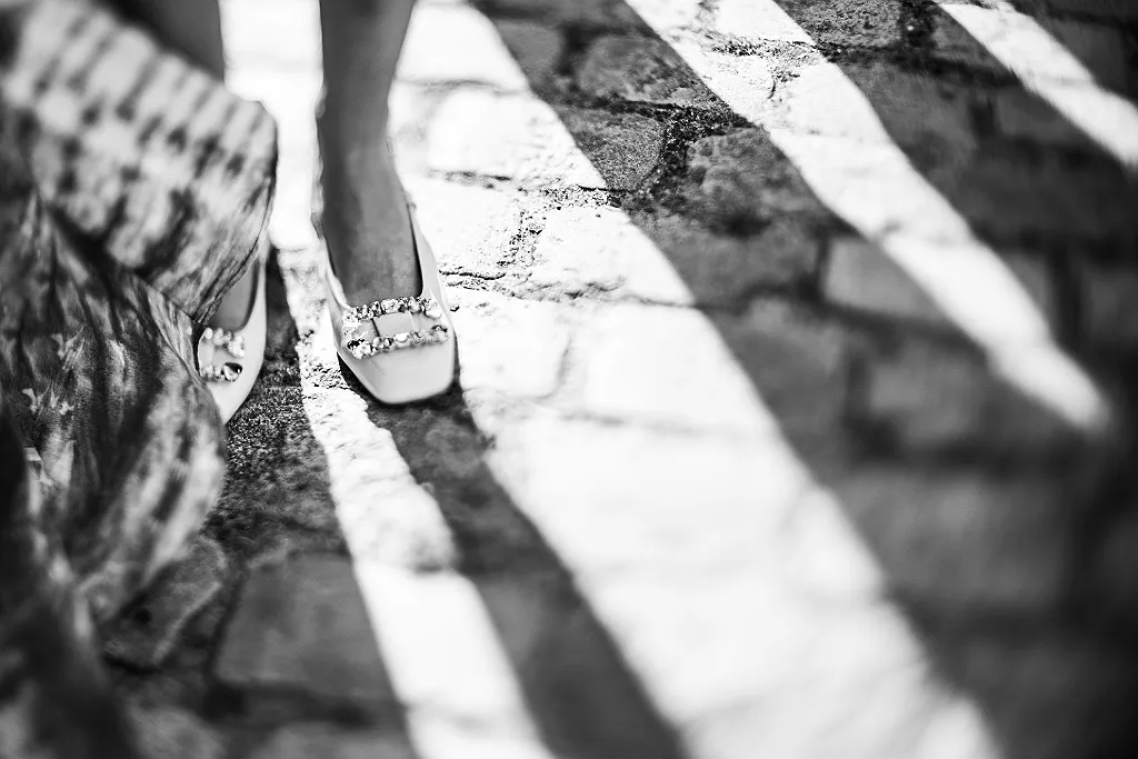 Hochzeitsbilder zeigen die Füße eines Brautpaares in flachen Schuhen auf einem gepflasterten Weg, Schwarz-Weiß.