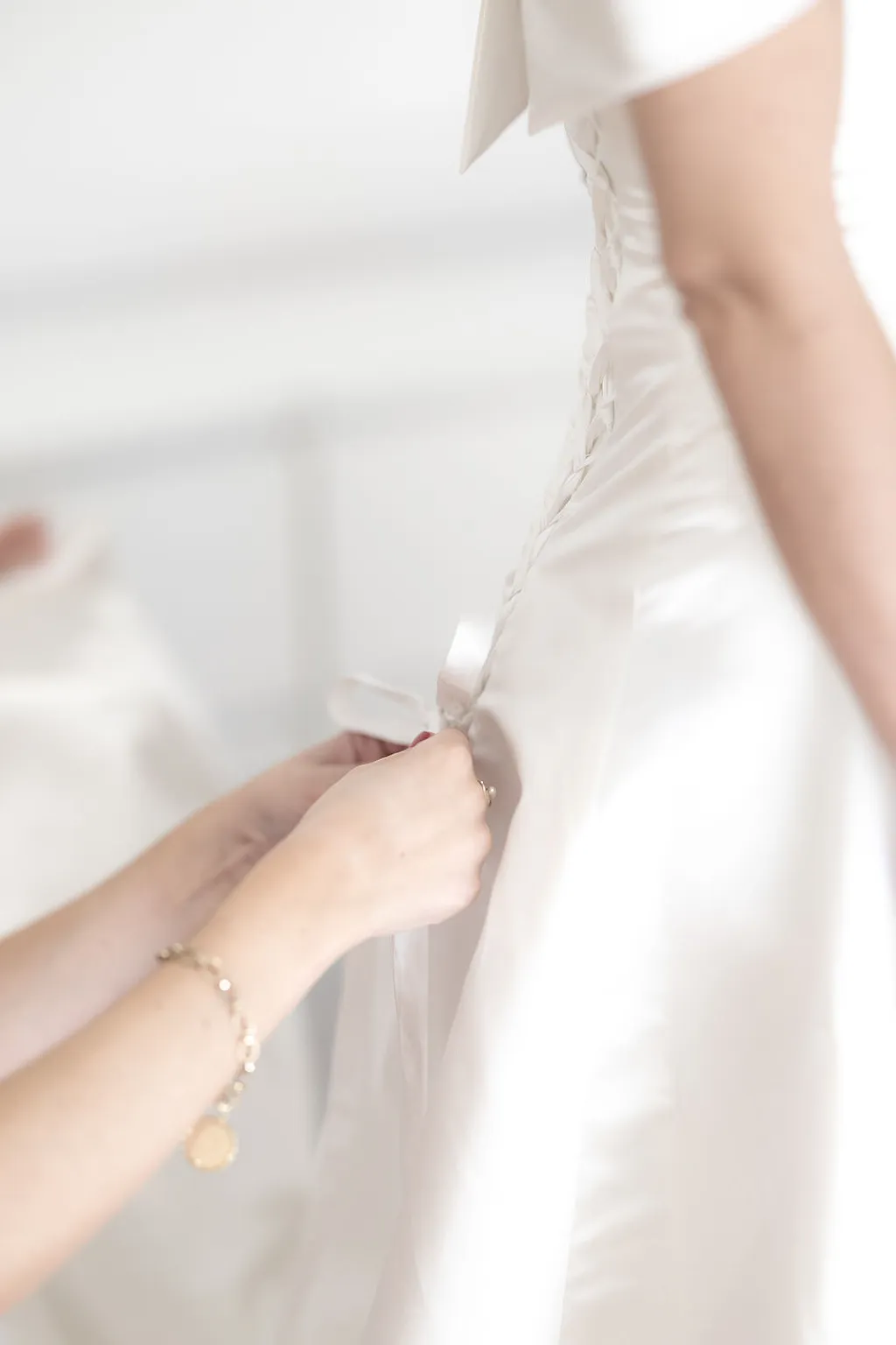 Hände schnüren ein weißes Satin-Hochzeitskleid am Rücken zu.