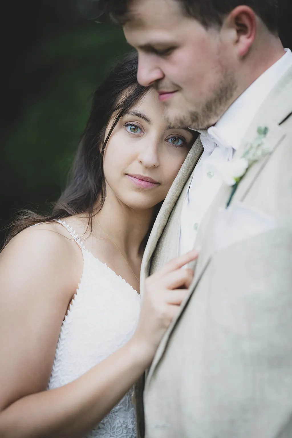 Eine Frau in einem weißen Kleid lehnt ihren Kopf an die Schulter eines Mannes im Hochzeitsanzug.