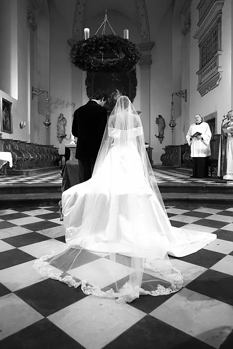 Brautpaar von hinten in Kirche, beide zum Altar gewandt, Priester rechts, Schachbrettboden.