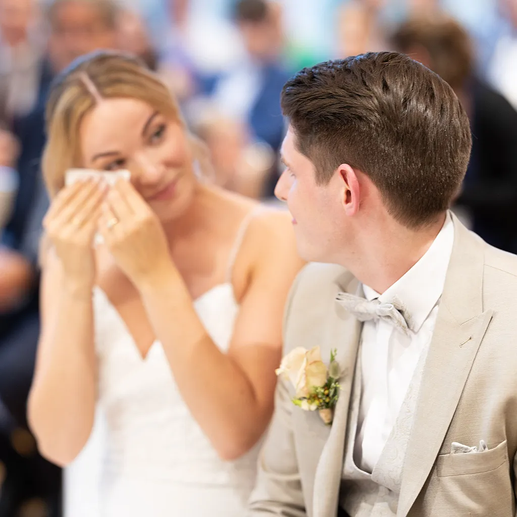 Eine weinende Frau im Hochzeitskleid mit einem Mann im Anzug daneben, der sie ansieht.