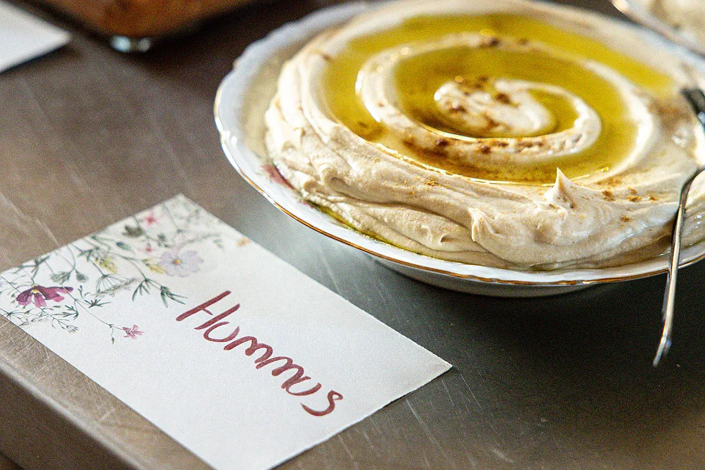 Eine Schale Hummus mit Olivenöl und ein Namensschild mit der Aufschrift "Hummus" darauf.