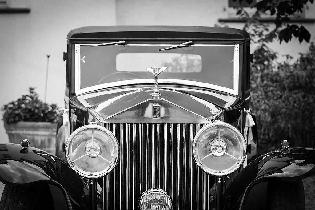 Frontansicht eines Oldtimer-Autos in Schwarz-Weiß mit Kühlerfigur, großem Kühlergrill und runden Scheinwerfern.