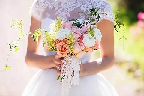 Eine Person in einem weißen Hochzeitskleid hält einen bunten Blumenstrauß mit weißen und rosafarbenen Blüten.