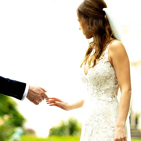 Eine Person in weißem Hochzeitskleid streckt die Hand aus zu einer weiteren Hand im dunklen Anzug.