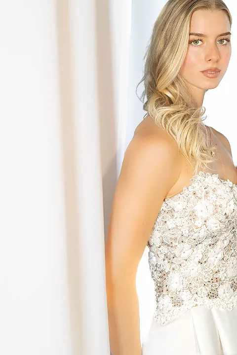 Blonde Frau im hochzeitskleid mit blick zur kamera, leicht seitlich von der linken seite angeschnitten.