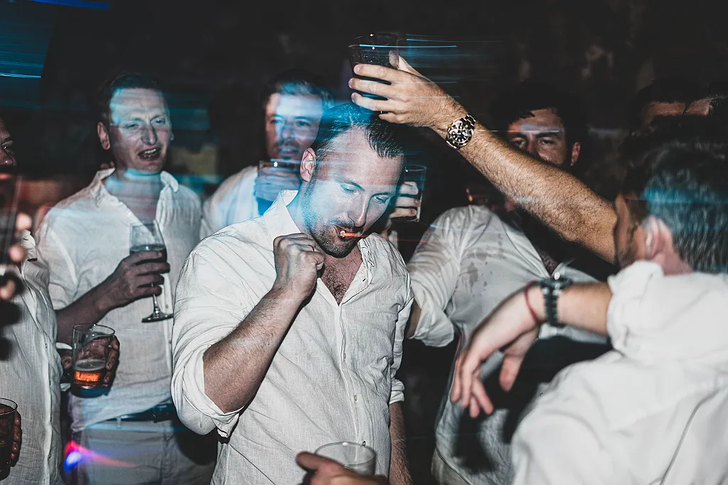 Gruppe Männer in weißen Hemden auf einer Party, blaues Licht und verschwommene Bewegungen.