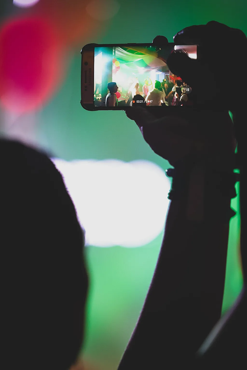 Ein Smartphone filmt eine Hochzeitsfeier mit bunten Lichtern und tanzenden Personen.