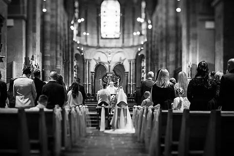 Hochzeitspaar und Gäste in einer Kirche, von hinten gesehen, während der Trauung, Schwarz-Weiß-Aufnahme.